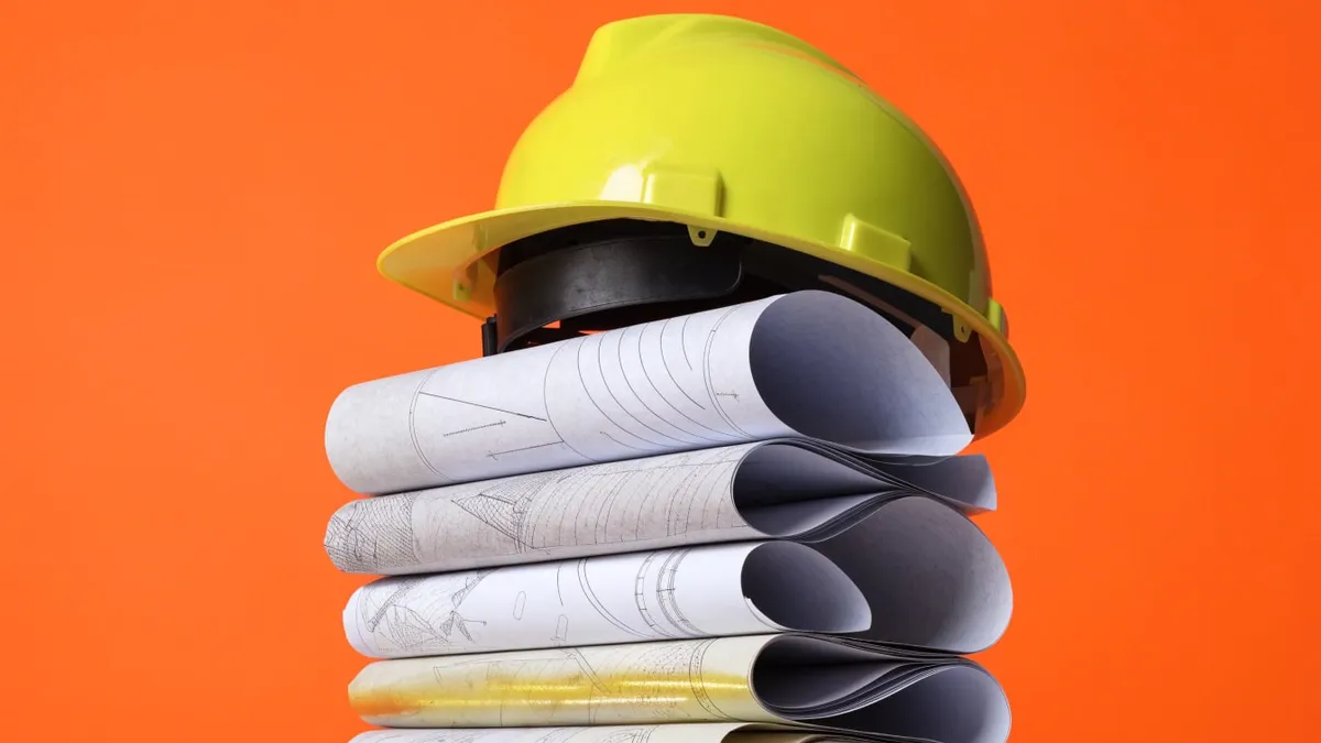 A hard hat resting on rolled site plans, cut out against a solid bright color.