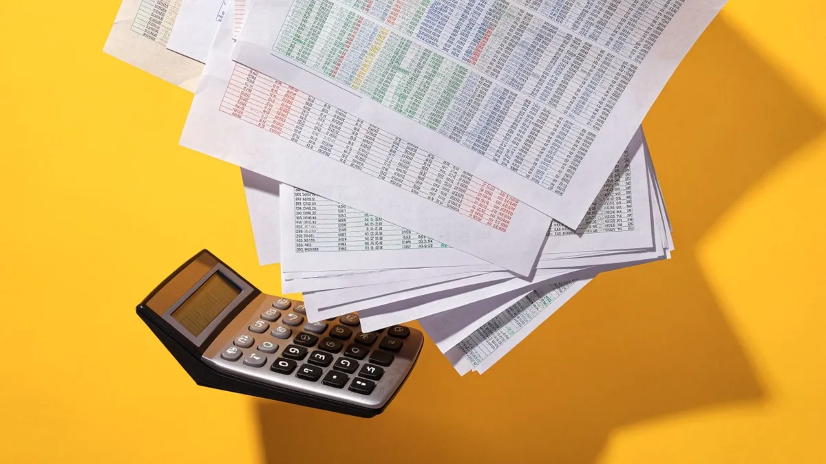 A calculator beside a stack of printed paper charts, cut out against a solid bright color.