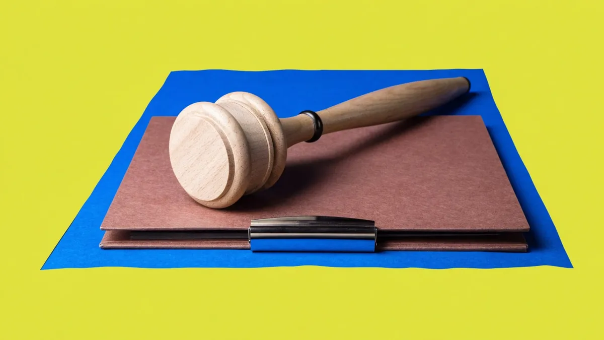 A wooden gavel resting on a closed folder, cut out against a solid bright color.