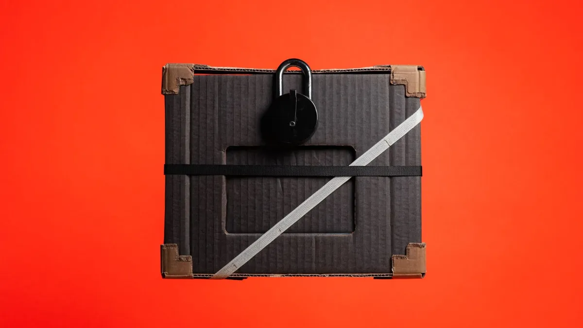 A black cardboard shipping box with a black padlock on top, wrapped in a black strap and a white diagonal strap, cut out against a solid red-orange background.