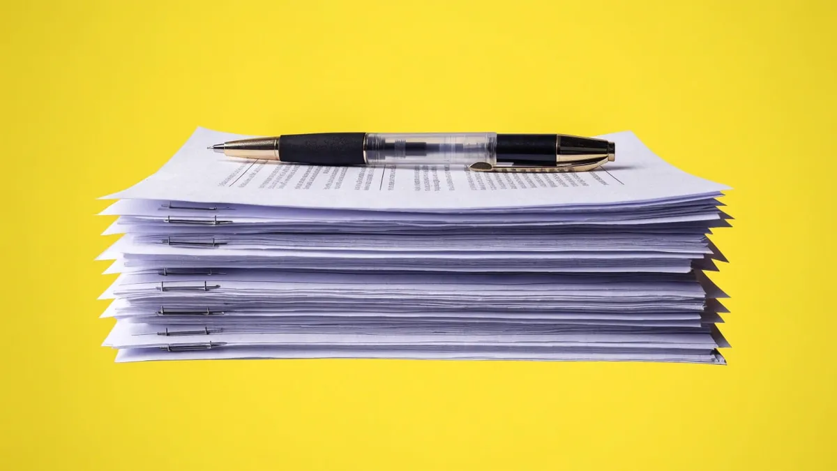 A stack of stapled papers with a pen resting on top, cut out against a solid bright color.